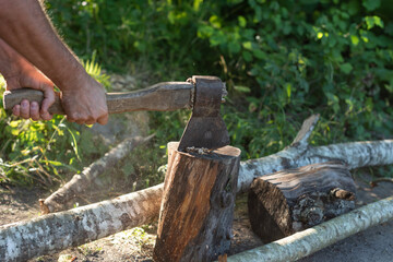 Male hands are holding an ax and chopping wood. One log flew off to the side.