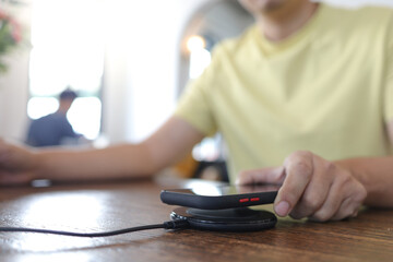 Charging mobile phone battery with wireless device in the table. Smartphone charging on a charging pad. Mobile phone near wireless charger.