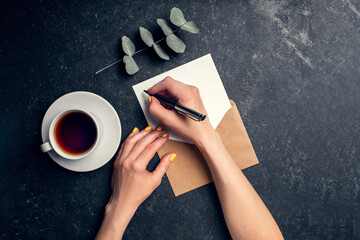 Woman writes letter on black background top view