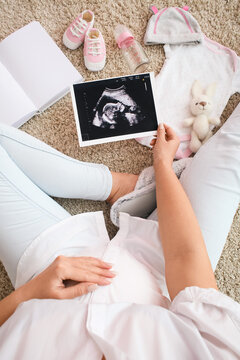 Pregnant woman with sonogram image and baby accessories on floor