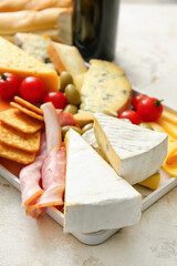 Tray with different types of cheese and snacks on light background, closeup