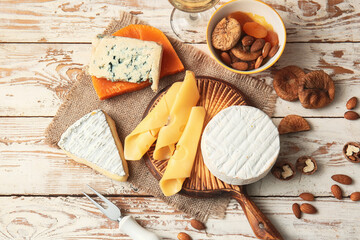 Different types of cheese, dried fruits and nuts on light wooden background
