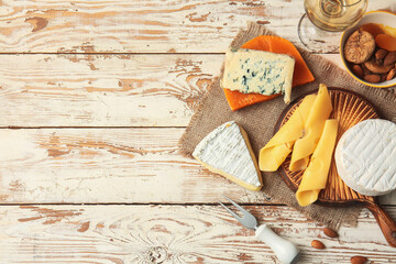 Different types of cheese, wine, dried fruits and nuts on light wooden background