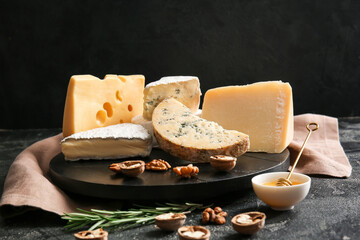 Tray with different types of cheese, walnuts and honey on dark background