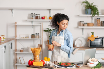 Young woman with mortar and pestle using laptop in kitchen