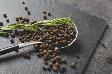 Spoon with peppercorns on dark background
