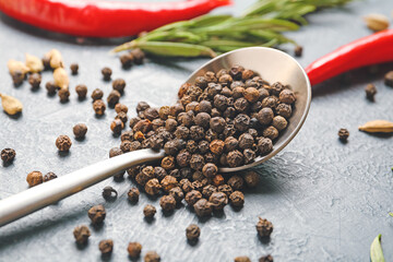 Spoon with peppercorns on color background