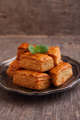 Baklava, traditional Turkish dessert. Crispy baklava on plate decorated with mint, on a old wooden background.