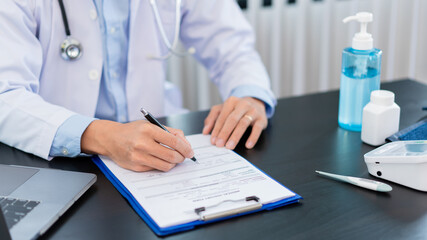 Medical concept a male doctor wearing a mask writing prescription to patient for recovering from Coronavirus (COVID-19) at his modern clinic