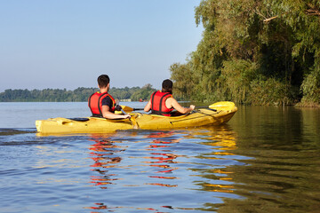 Mother and big son paddle yellow kayak on Danube river. Summer kayaking. Concept for family, adventure, travel, action, lifestyle and kayaking