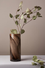 Still life photo of branches with green leaves placed into cylindric brown marble vase made in...