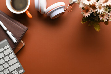 Above view stylish workspace with notebook, headphone, coffee cup and flowers on brown leather.