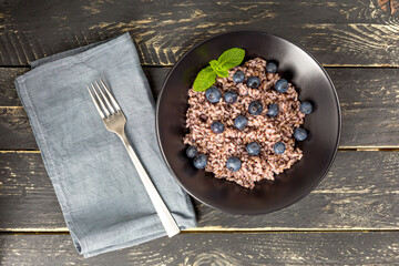 Delicious risotto with blueberries served on dark wooden table, flat lay