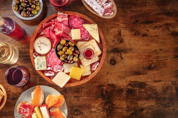 Charcuterie and cheese platter with wine, top shot on a rustic background with copy space. Italian antipasti or Spanish tapas, shot from above with olives and salmon sanwiches