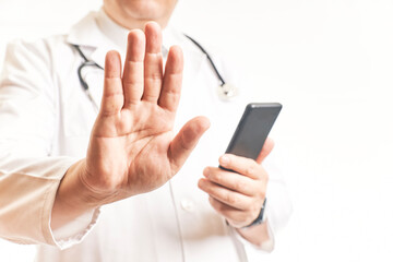 Doctor placing his palm with the Stop gesture consulting the cell phone to view patient data