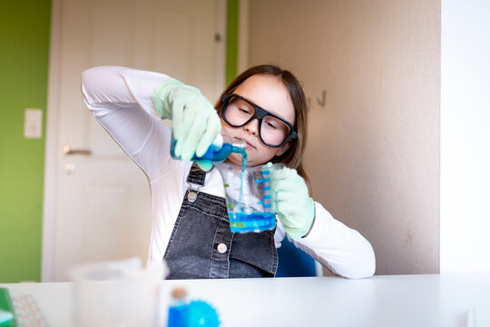pretty young schoolgirl sitting on her desk in room at home experimenting with blue liquid while homeschooling chemistry during corona time - Powered by Adobe