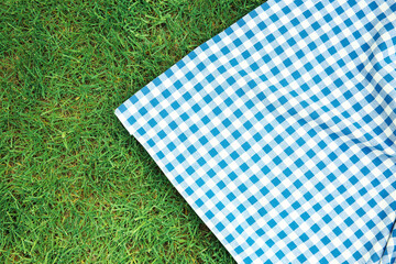 Blue checkered picnic cloth on green grass top view. Checkered towel country design backdrop. Food advertisement display