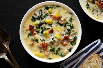 Homemade Zuppa Toscana with Kale and Bread in a white bowl on a black background, top view. Overhead, from above, flat lay.