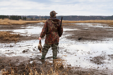 a hunter stands on a mud bank with a downed duck in his hand