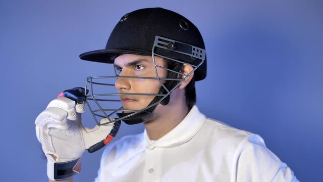 Young Indian Cricketer Adjusting His Helmet In The Dressing Room - Getting Ready For The Game. Closeup Shot Of A Confident Cricket Player With Gloves And Helmet Posing For The Camera - Active Sports