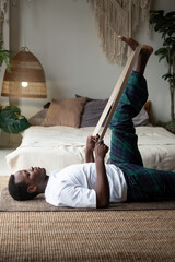Young sporty african man working out at home , warming up using yogic belt