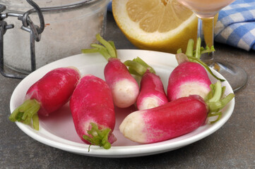 Radis dans une assiette à côté d'un verre de vin, d'un citron et d'un pot de sel