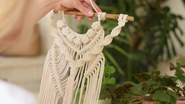A blonde woman weaving macrame from light threads in a home workshop.Handmade concept.Slow motion.