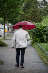 Portrait on back view of man walking in the street with a red umbrella in hand