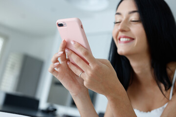 Young woman grinning happily to herself as she uses a smartphone