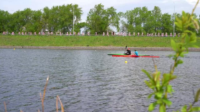 Kayak athletes compete with each other on the river in sunny weather in calm water. 4K video.