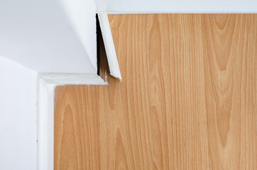 Naklejka na ściany i meble Breaking white skirting board at the corner on parquet or wooden floor.