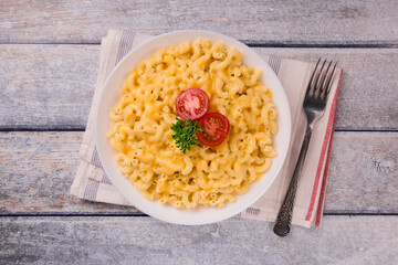 Macaroni and cheese on a white plate with parsley and cherry tomatoes on a wooden background