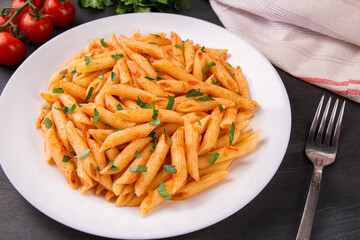 Penne pasta in tomato sauce, decorated with parsley on a black background
