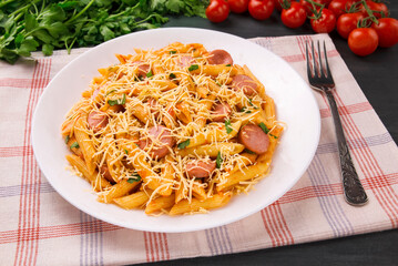 Penne pasta in tomato sauce with sausages and cheese, decorated with parsley on a  black background