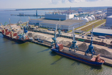 An aerial drone view of the industrial port in the Baltic Sea. There is a ships under load in the harbor.	