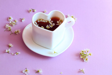 A cup of tea in the form of a heart with scattered petals of white delicate flowers on a pastel background, side view, space for text