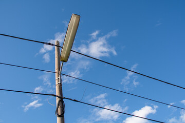 A street lamppost with wires. Wooden pole with a lantern and electric cables against a blue sky.