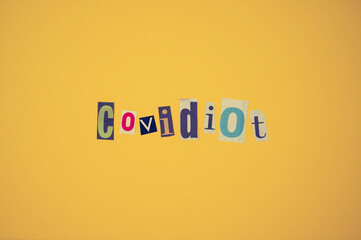 Ausgeschnittene Zeitungsbuchstaben auf neutralem Hintergrund bilden das Wort Covidiot