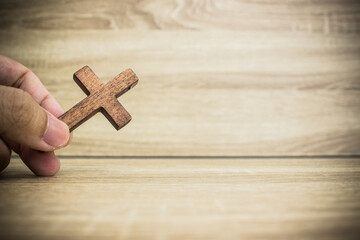Hand holding a wooden cross over the wooden background. 