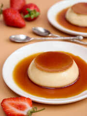 A caramel custard pudding with vanilla flavor in a white plate with strawberries. Dessert base with caramelized sugar layer toppings which is made of eggs, sugar, milk who are the main ingredients