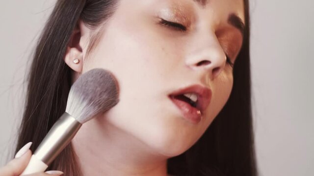 Smooth skin care. Female beauty. Natural look. Nude makeup. Pretty brunette woman applying cosmetic brush for compact face powder looking at camera isolated neutral.