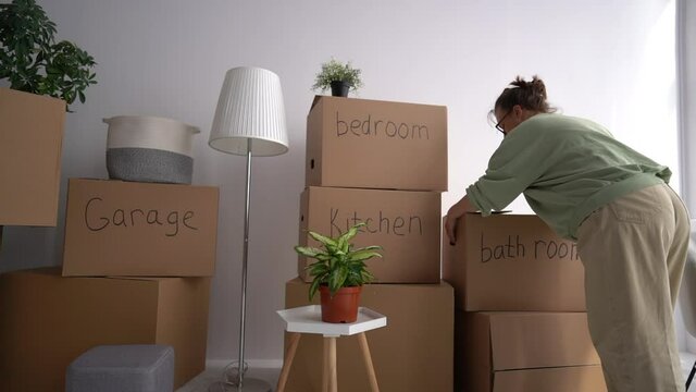 Moving, relocation and minimalism concept. A woman brings cardboard boxes with the inscriptions garage, kitchen, living room, bedroom, bathroom to her new home