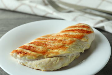 Plate with grilled chicken breast on gray textured table