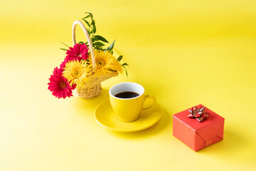 Obraz na płótnie Canvas 贈り物とコーヒーとヒマワリのような細い花びらの黄色のガーベラ（イエロースパイダー）と赤のガーベラの花かご