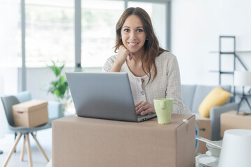 Happy woman moving in her new house and using her laptop