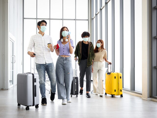 Asian young tourist group with luggage wearing face mask to prevent coronavirus infection, standing...