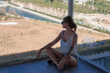 blond girl traveler in sunglasses posing on background of Athens in panoramic glass corridor of contemporary building