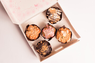 closeup of colorful muffins and cupcakes box isolated on white background. muffins with chocolate and sugar glaze and icing, concept of sugar consumption