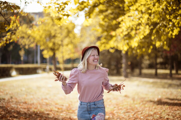 Young smiling blond woman enjoying in the park and holding leaves.