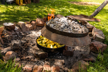Cooking traditional dalmatian, croatian, bosnian dish called peka. Meat, potatoes and vegetables in pot and covered with hot charcoal and ash. Balkan food. - obrazy, fototapety, plakaty
